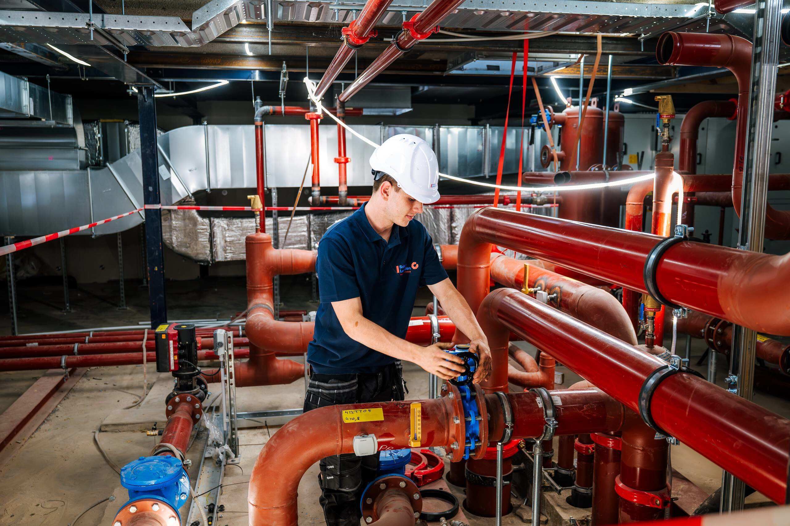 Monteur met helm werkt aan leidingwerk in een technische ruimte